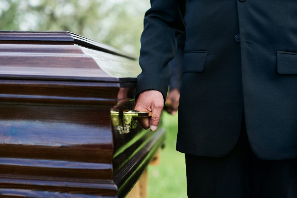 Close-up of man in black suit holding by handle of wooden coffin
